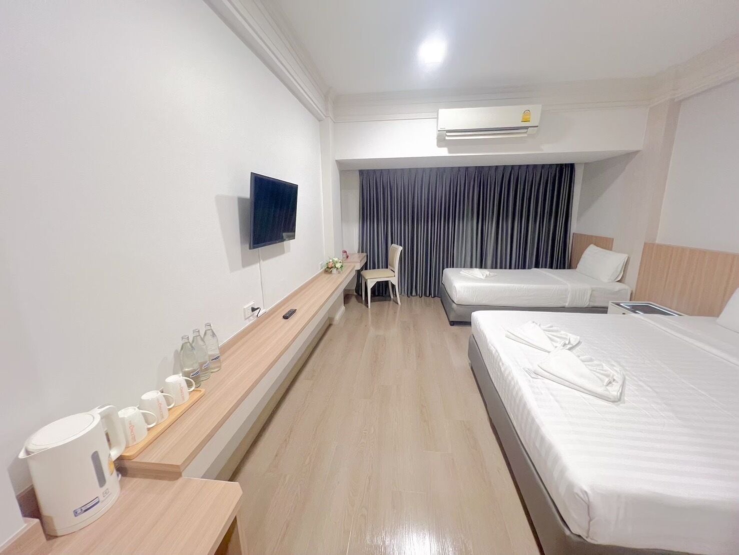 A hotel room with a TV, two beds, a desk with a coffee maker, and an air conditioner.