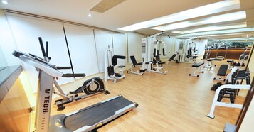 Un gimnasio con diverso equipo de ejercicio, que incluye cintas de correr, elípticas y bancos de pesas.
