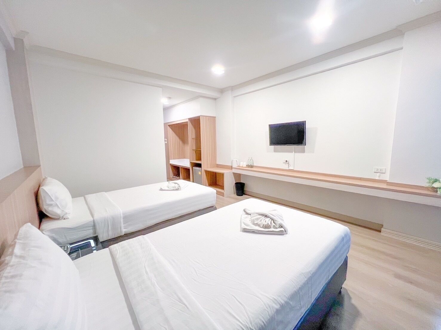 A hotel room with two beds, a TV mounted on the wall, and a wooden cabinet.