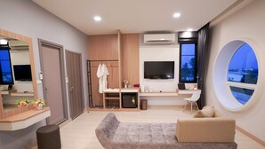 Una habitación de hotel moderna con sofá, televisor, escritorio, espejo y un amplio ventanal con vistas.