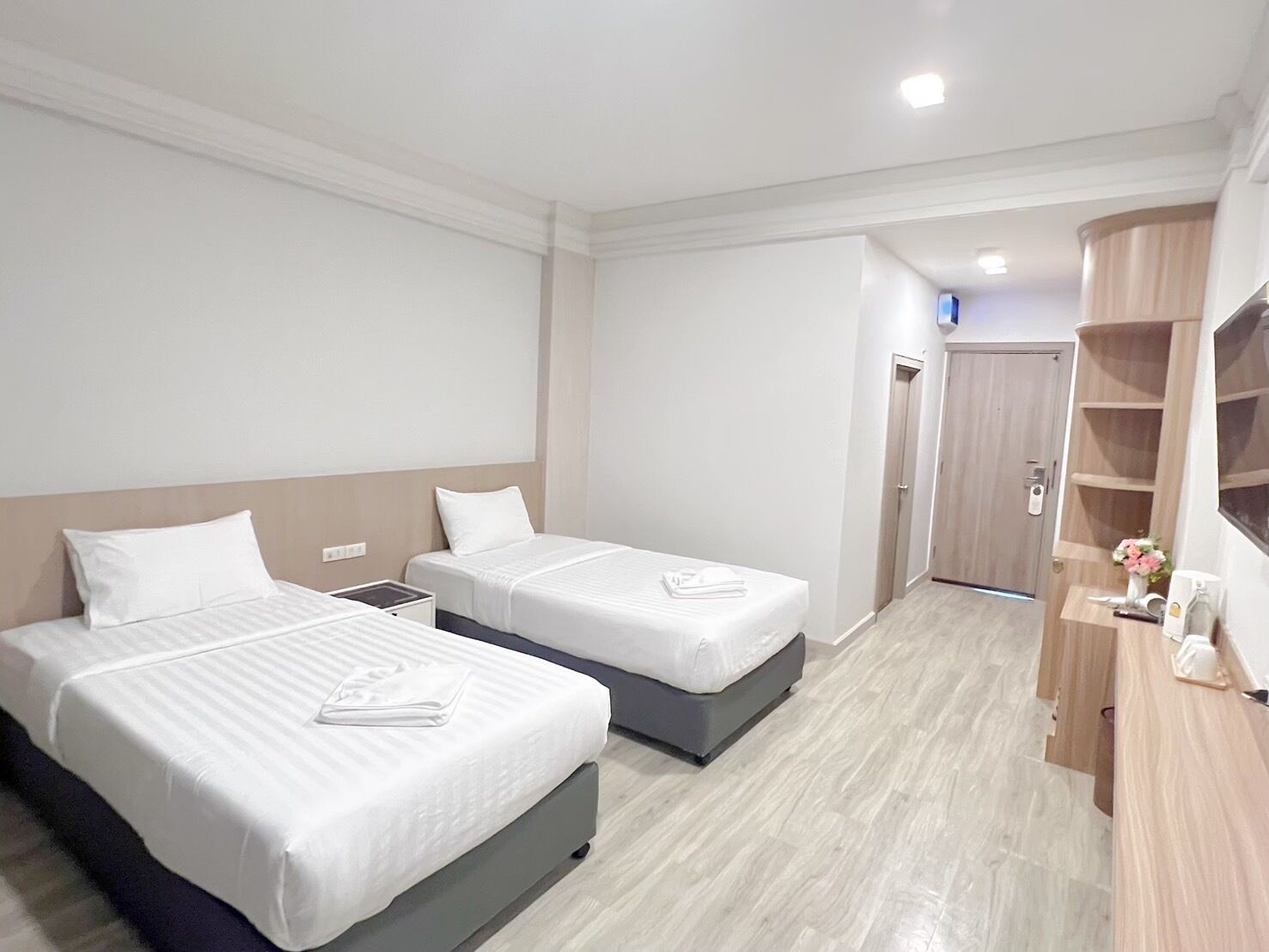 A hotel room with two beds, a wooden wardrobe, and a small desk with a vase of flowers.