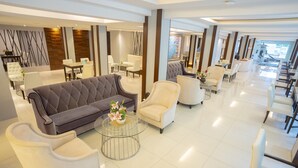 Un moderno vestíbulo de hotel con diversas zonas de estar, incluyendo sofás y sillones, dispuestas alrededor de una mesa de centro con flores.