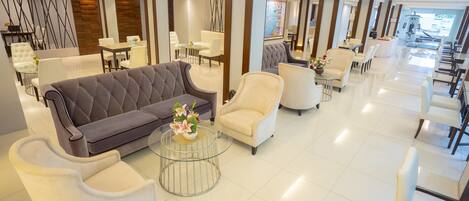 Una hall d'albergo moderna con diverse zone relax, tra cui divani e poltrone, disposte attorno a un tavolino da caffè con fiori.