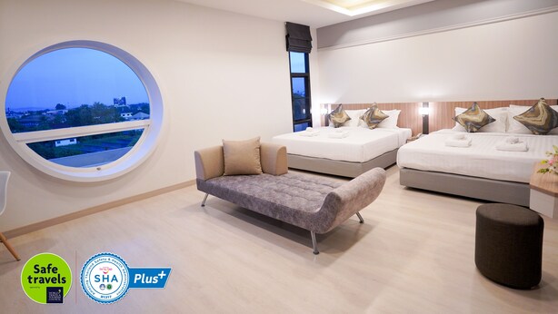 Una habitación de hotel moderna con un ventanal redondo grande, dos camas, un sofá y un pequeño otoman.