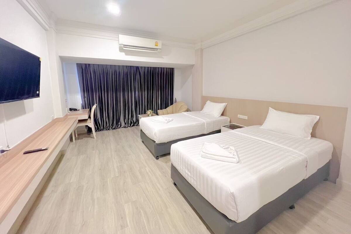 A hotel room with two beds, a desk, a chair, and a TV.