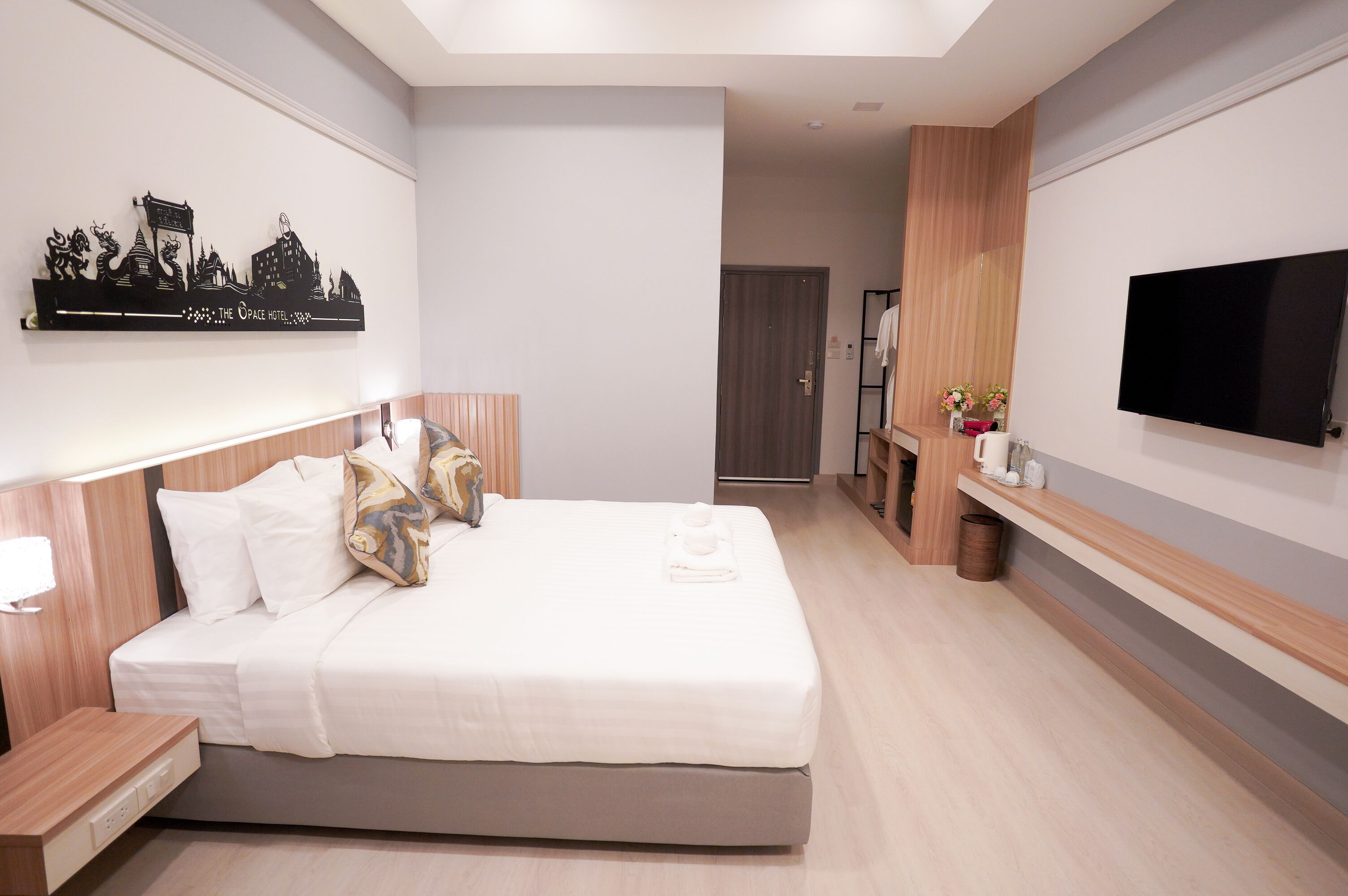 Una habitación de hotel moderna con cama, mesita de noche, televisor montado en la pared y una obra de arte decorativa con un paisaje urbano.