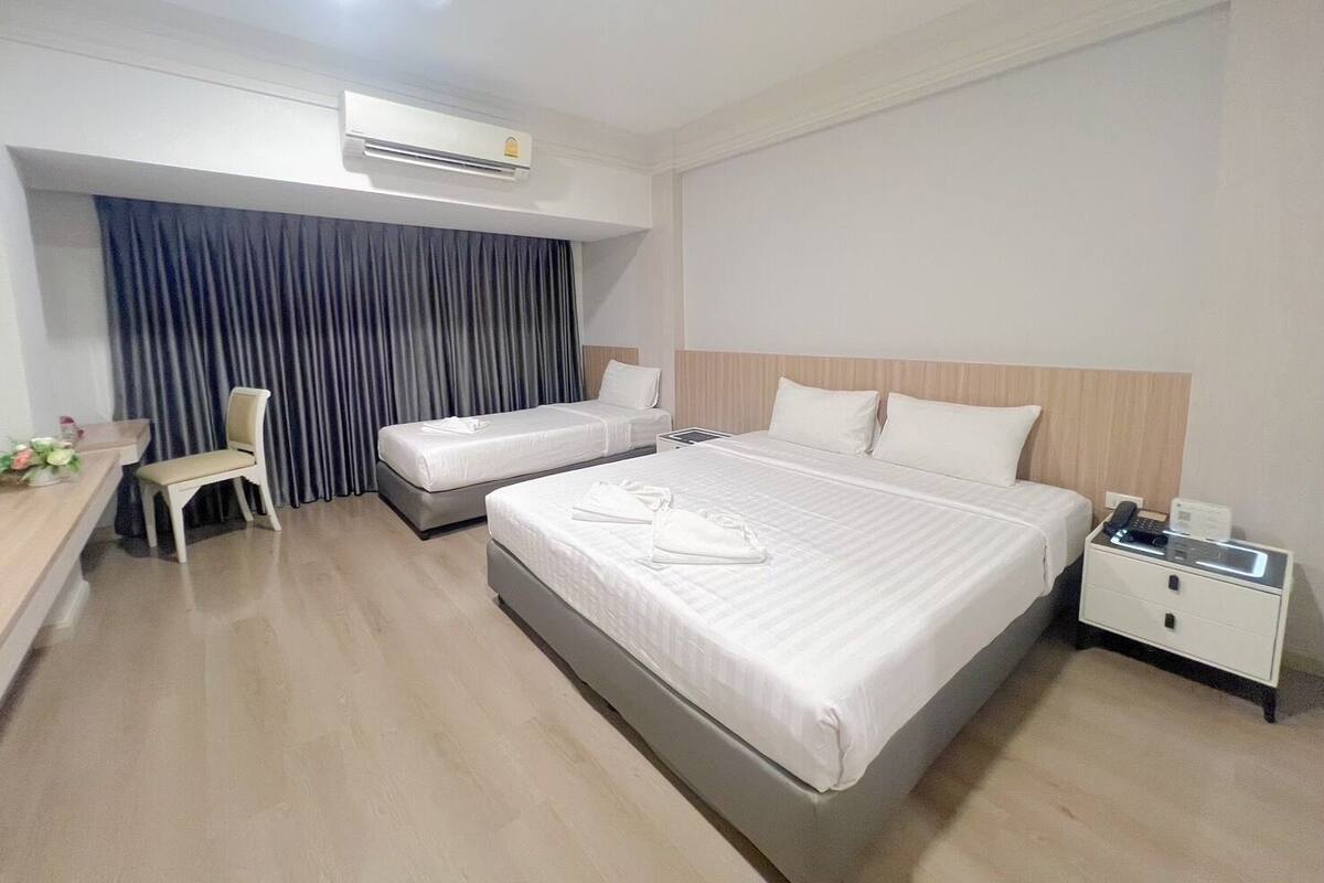 A hotel room with two single beds, a desk with a chair, a bedside table with a phone, and an air conditioning unit.