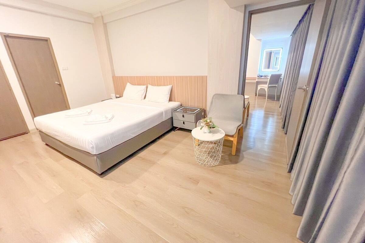 A modern hotel room with a large bed, a bedside table, a chair, and a small round table with a vase.