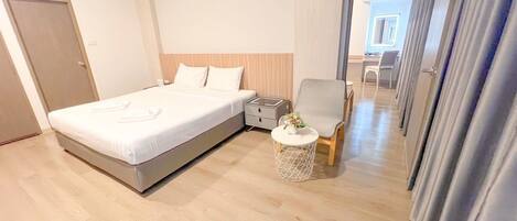 Quarto de hotel moderno com uma cama grande, uma mesinha de cabeceira, uma cadeira e uma pequena mesa redonda com um vaso.