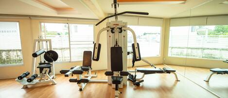 A gym with various exercise equipment, large windows, and wooden flooring.
