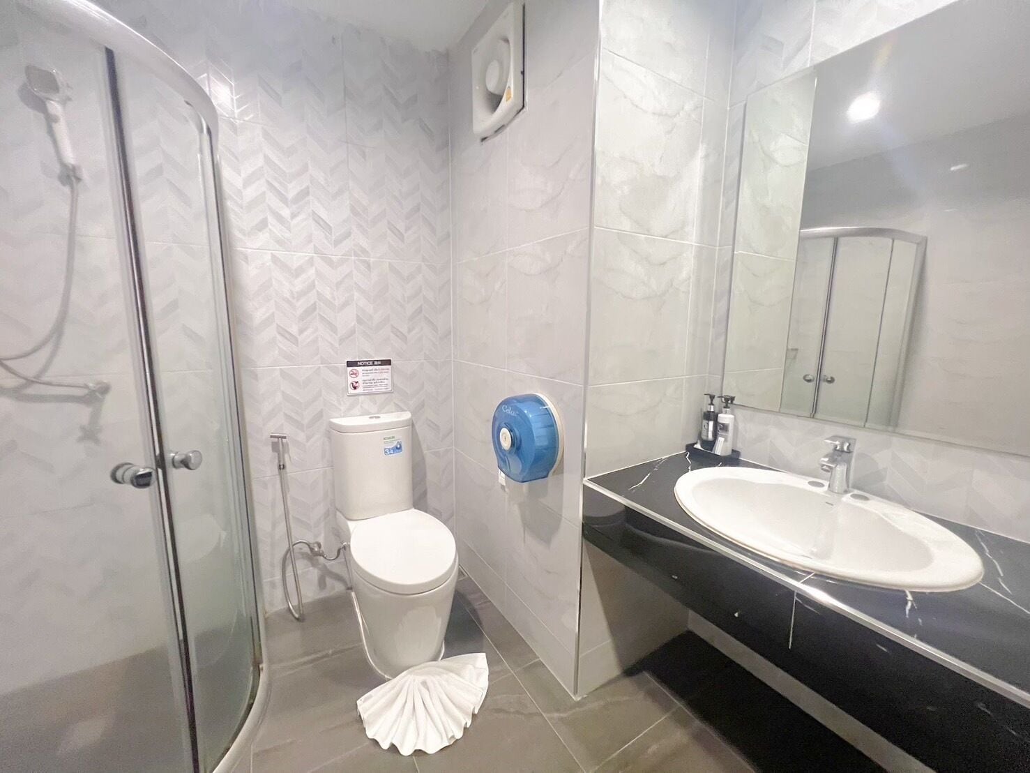 A bathroom with a glass shower enclosure, a toilet, a bidet, and a sink with a black countertop.