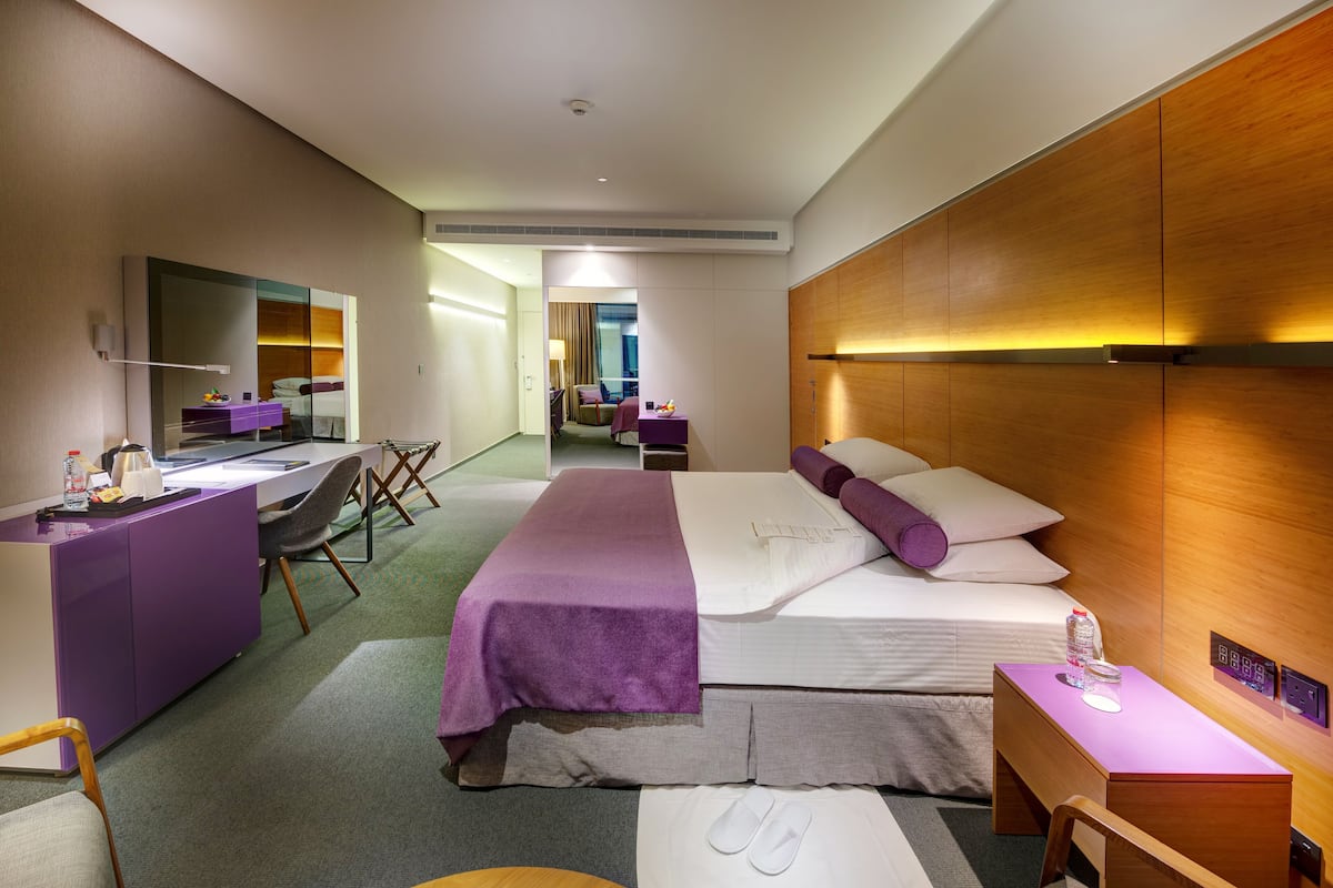 A modern hotel room with a large bed, a desk, a chair, and a mirror.