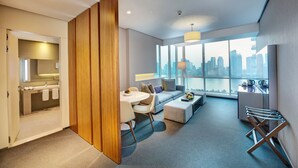 A modern hotel room with a dining area, a sofa, a small table, and a view of the city skyline through large windows. - The Act Hotel Sharjah (Sharjah)