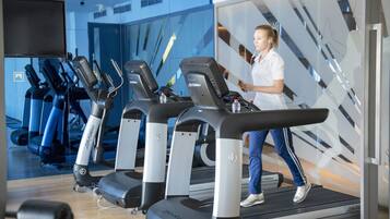 A gym with treadmills, a mirrored wall, and a person walking on a treadmill.