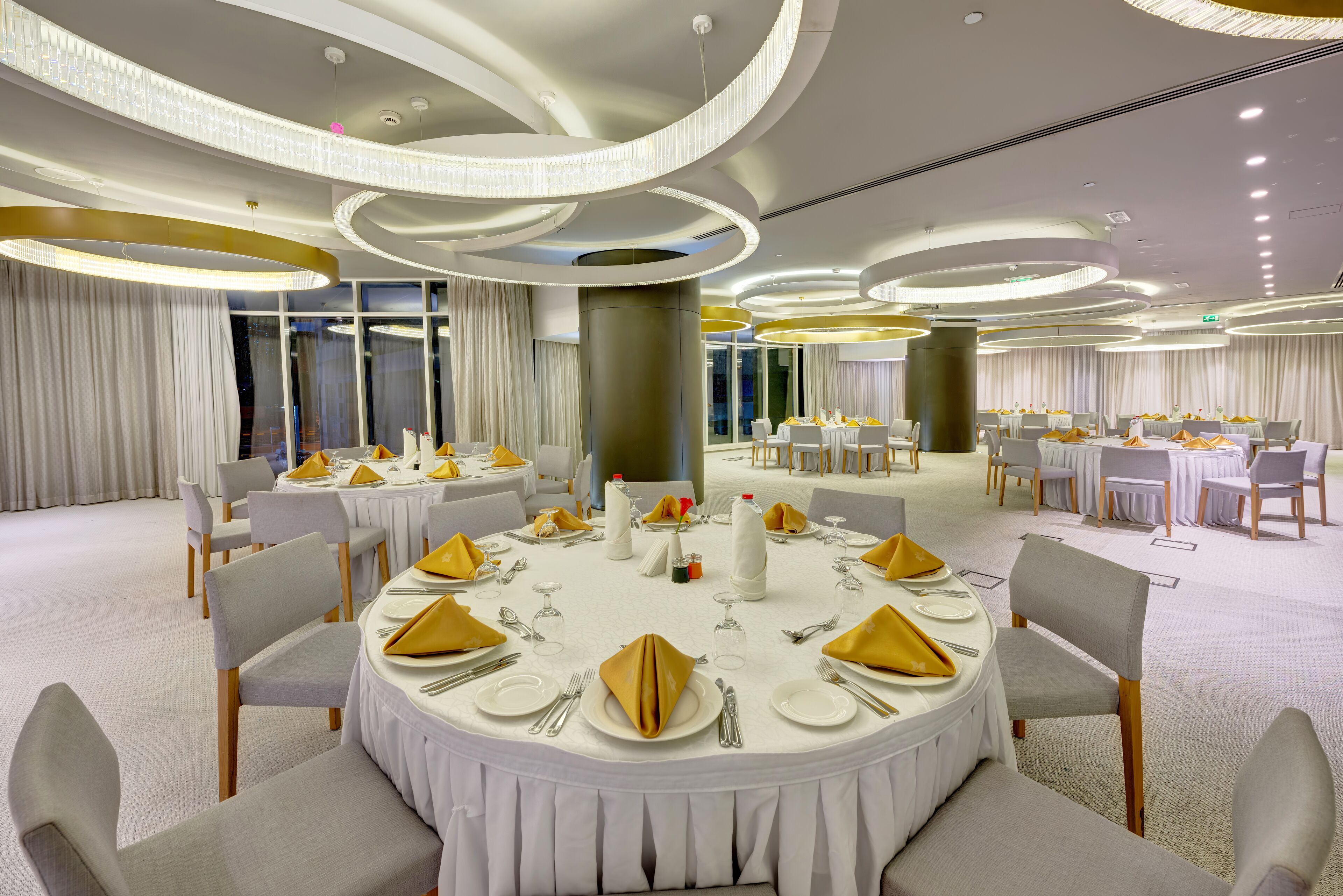 Une salle de banquet avec des tables rondes dressées pour le repas, ornées de nappes blanches et de serviettes dorées.