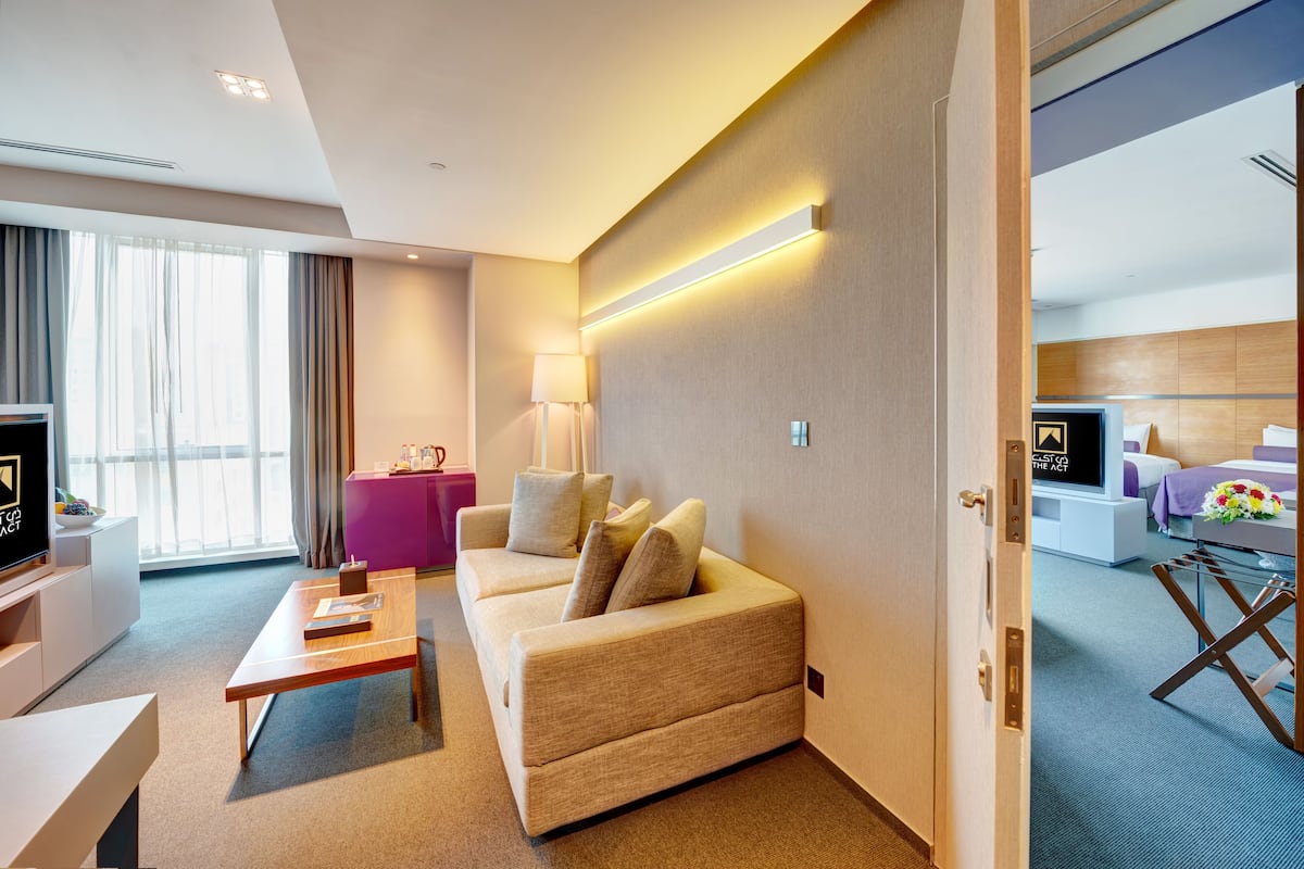 A modern hotel room with a sofa, a coffee table, a TV, a desk, and a pink side table.