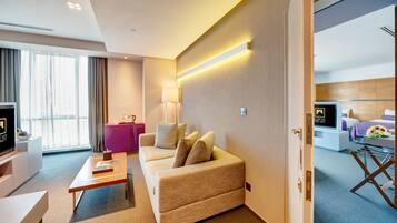 A modern hotel room with a sofa, a coffee table, a TV, a desk, and a pink side table.