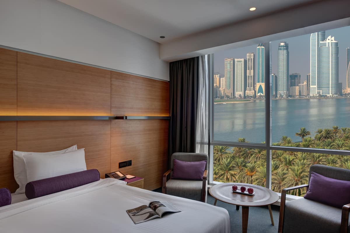 A hotel room with a large bed, a view of the city skyline, and a palm tree view.