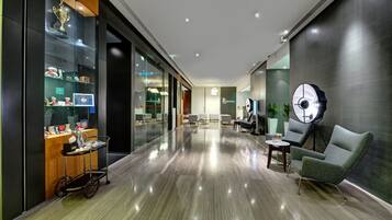 A modern hotel lobby with a polished floor, a reception desk, seating area, and a trophy display.