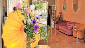 A room with a large yellow umbrella centerpiece, a pink sofa, and a glass table with three glasses.