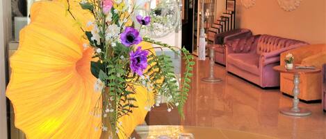 A room with a large yellow umbrella centerpiece, a pink sofa, and a glass table with three glasses.