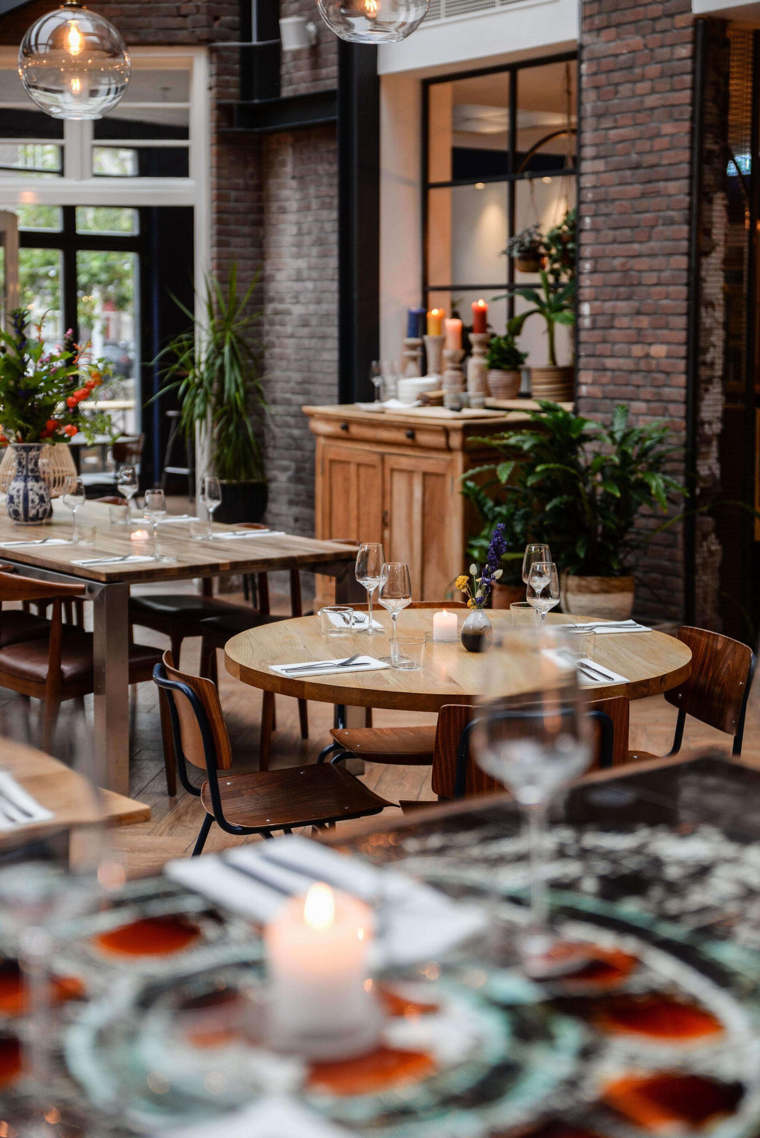 Un restaurante con mesas redondas, velas y plantas en macetas.