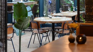 An indoor dining area with large windows, wooden tables, and hanging pendant lights.