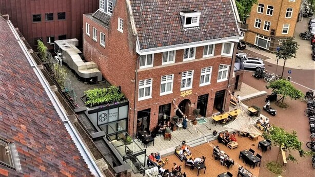 A building with a courtyard featuring outdoor seating, a visible restaurant, and a clock tower.