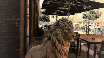 A lion statue on a pedestal in an outdoor seating area with tables and umbrellas.