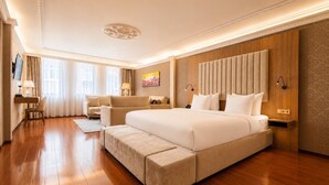 A spacious bedroom with a large bed, a sofa, a desk, and a television.