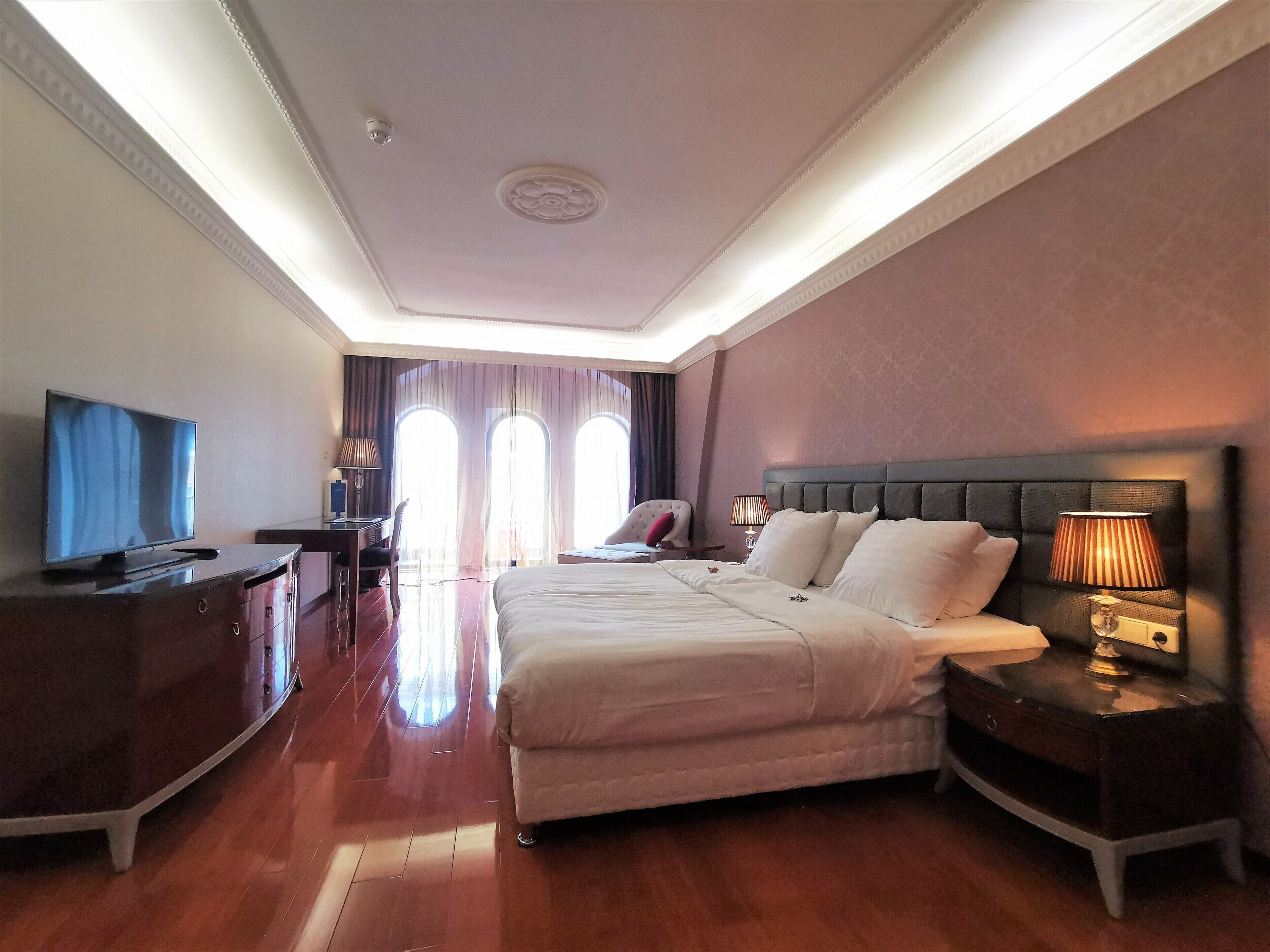 A hotel room with a large bed, a desk, a TV, and a nightstand with a lamp.