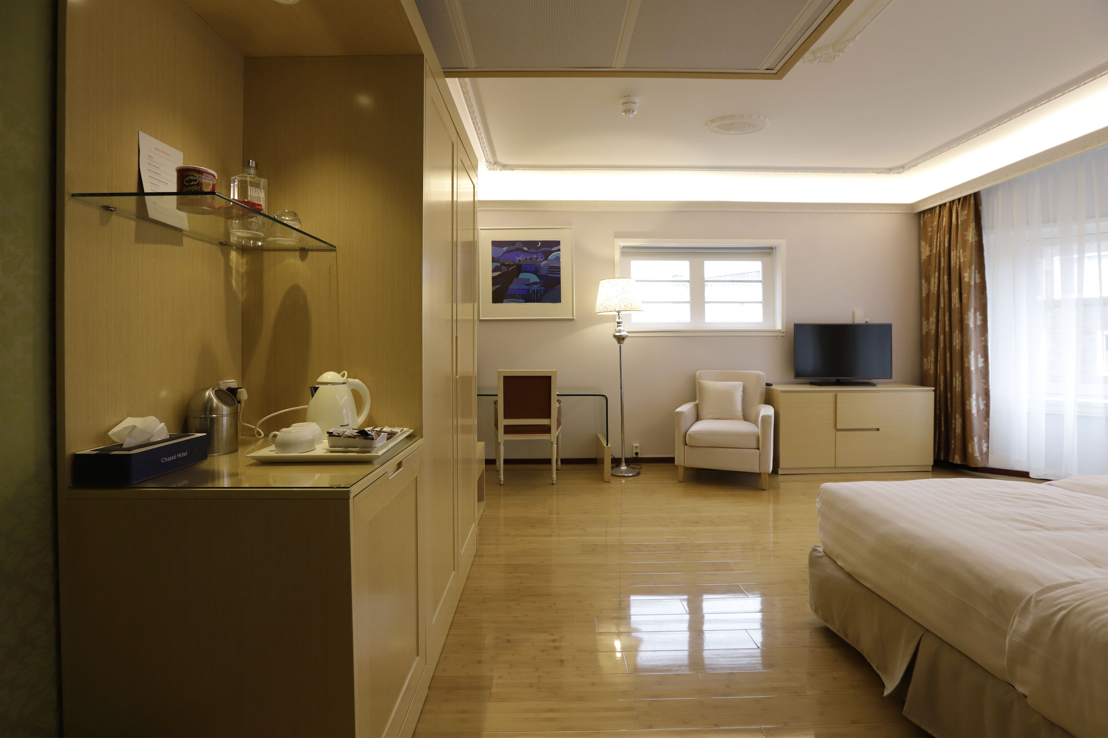 A hotel room with a bed, a desk with a lamp, a chair, a television, and a window with curtains.