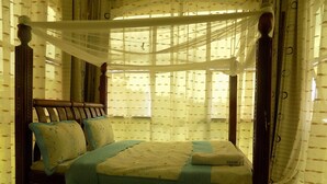 Una cama con dosel y dos columnas, con un edredón estampado con motivos florales, un cabecero de madera y una mesita de noche con lámpara.