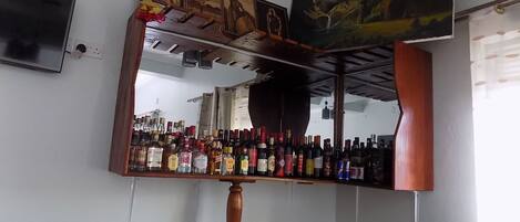 Zona de bar con mostrador de madera, un espejo grande y varias botellas de licores.