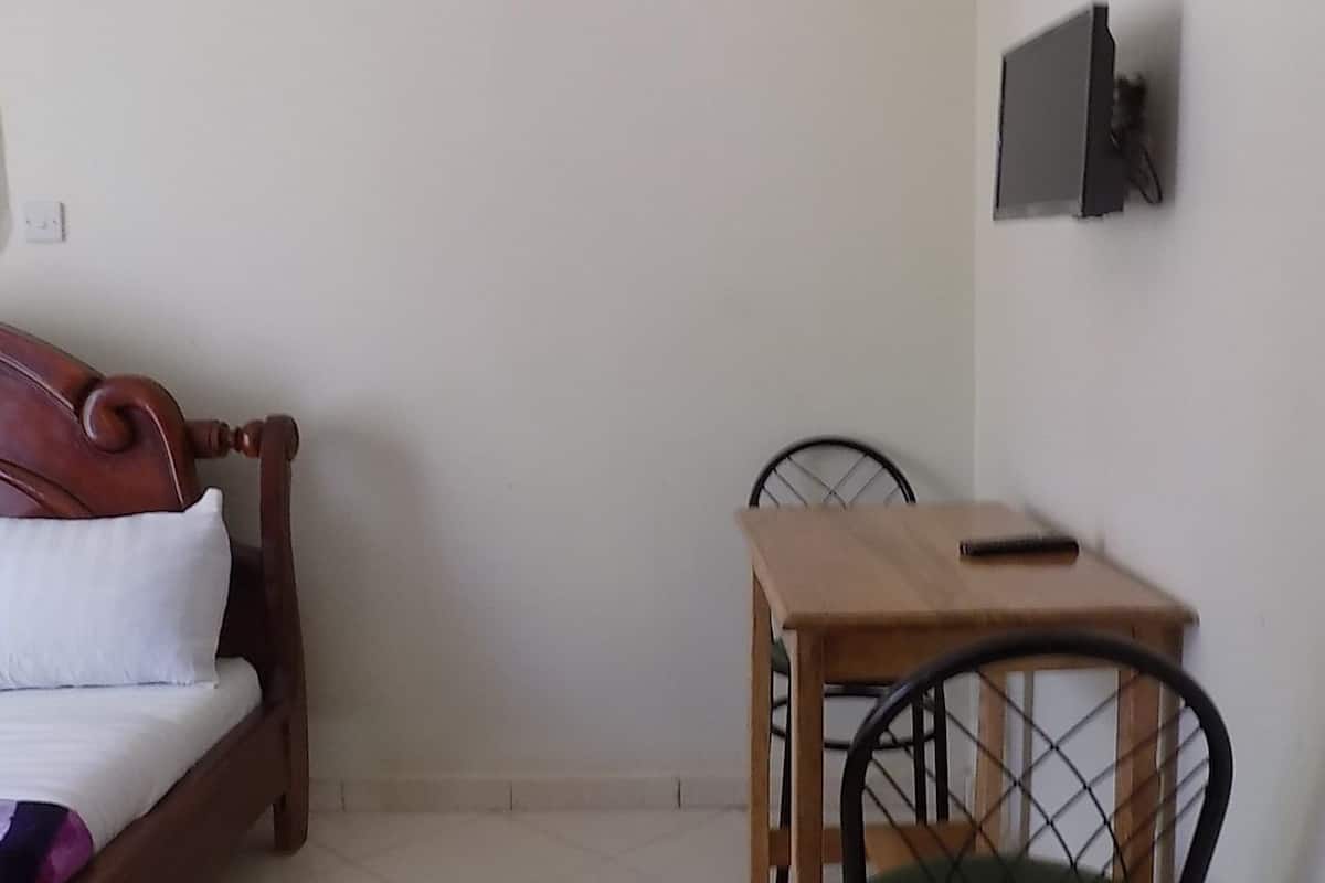 Un dormitorio con una cama de madera, una mesita de madera, una silla y un televisor montado en la pared.