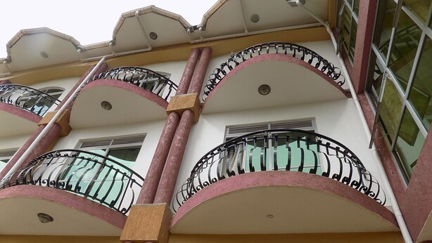 Un edificio de varios pisos con balcones y barandillas de hierro forjado, y fachada de color rosa parduzco.