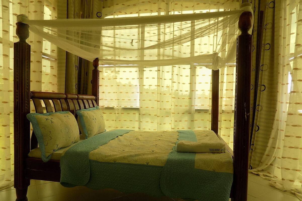 Una cama con dosel y cuatro columnas, con un edredón estampado con motivos florales, un cabecero de madera y cortinas de encaje.