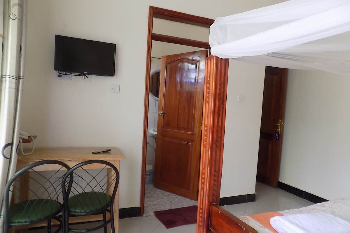 Una habitación con una cama, un escritorio con una silla, una televisión y una puerta que da a otra habitación.