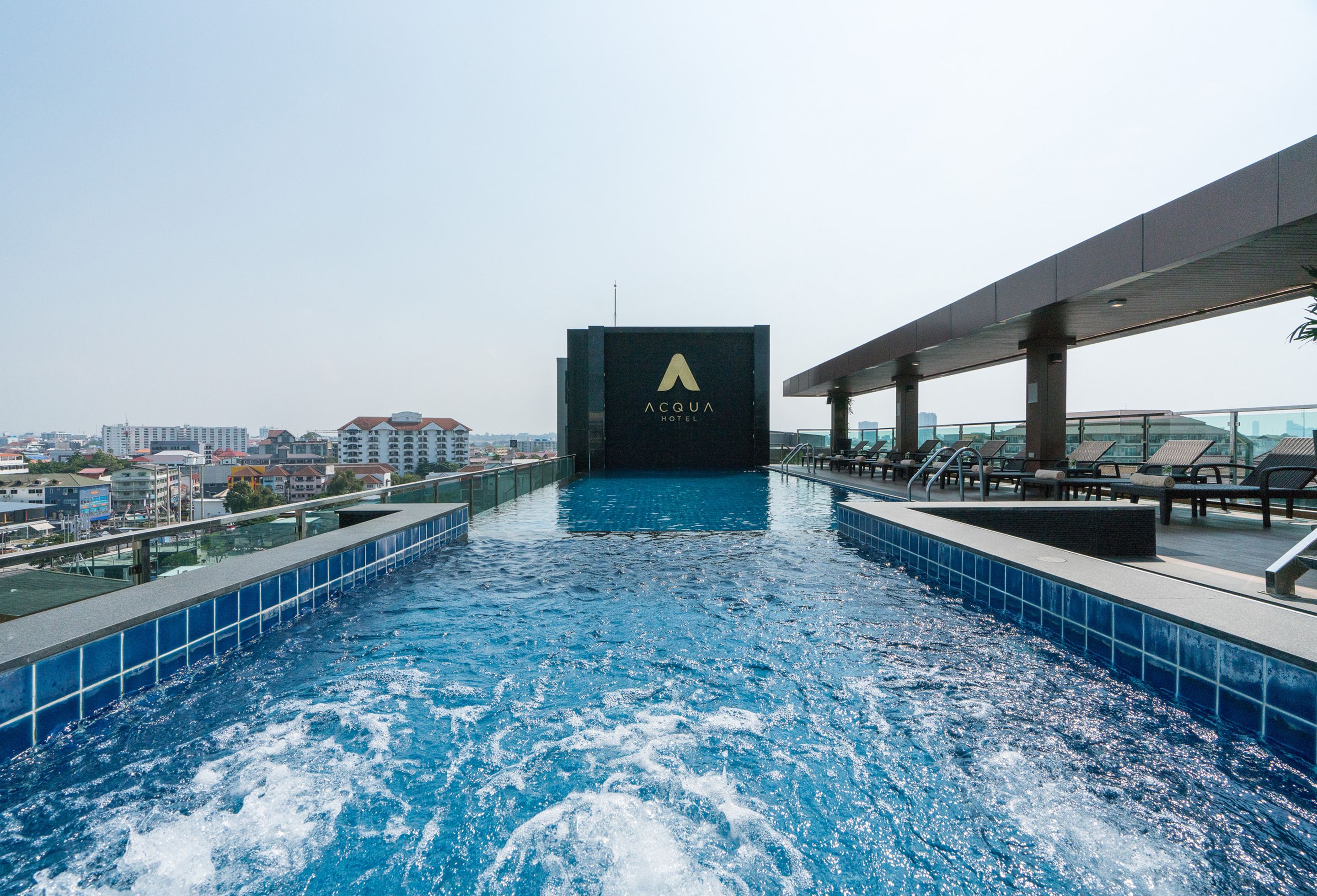 Een dakzwembad met een panoramisch uitzicht op de stad, een bord met daarop Acqua Hotel, en ligstoelen langs het zwembad.