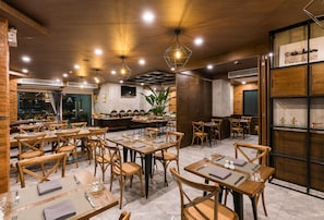 Un restaurant avec des tables et des chaises en bois, un coin bar et une grande plante en pot.