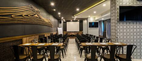 A conference room with a long table, chairs, a projector screen, and a patterned wall.