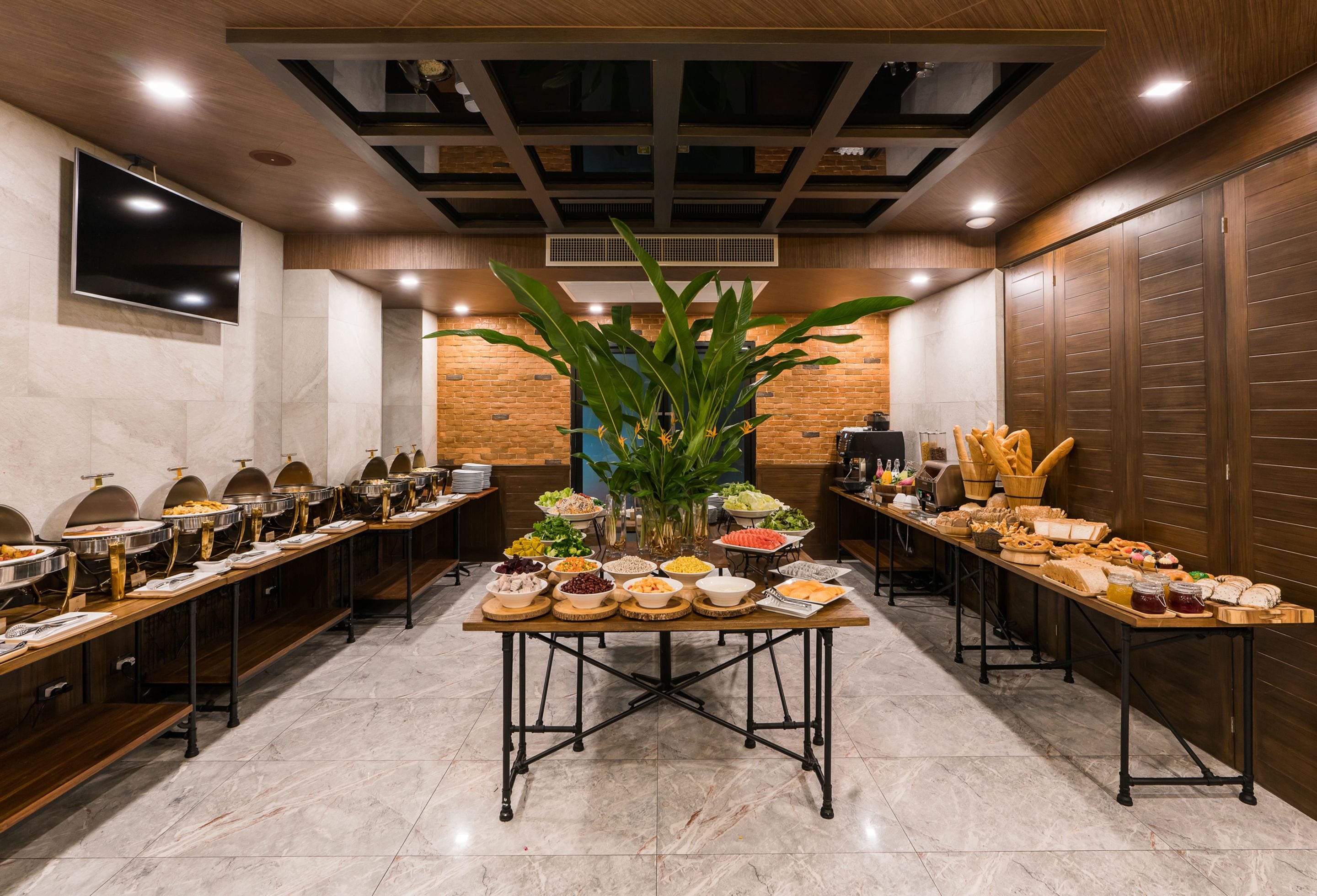 A buffet setup with multiple food stations, a large plant centerpiece, and a modern ceiling design.