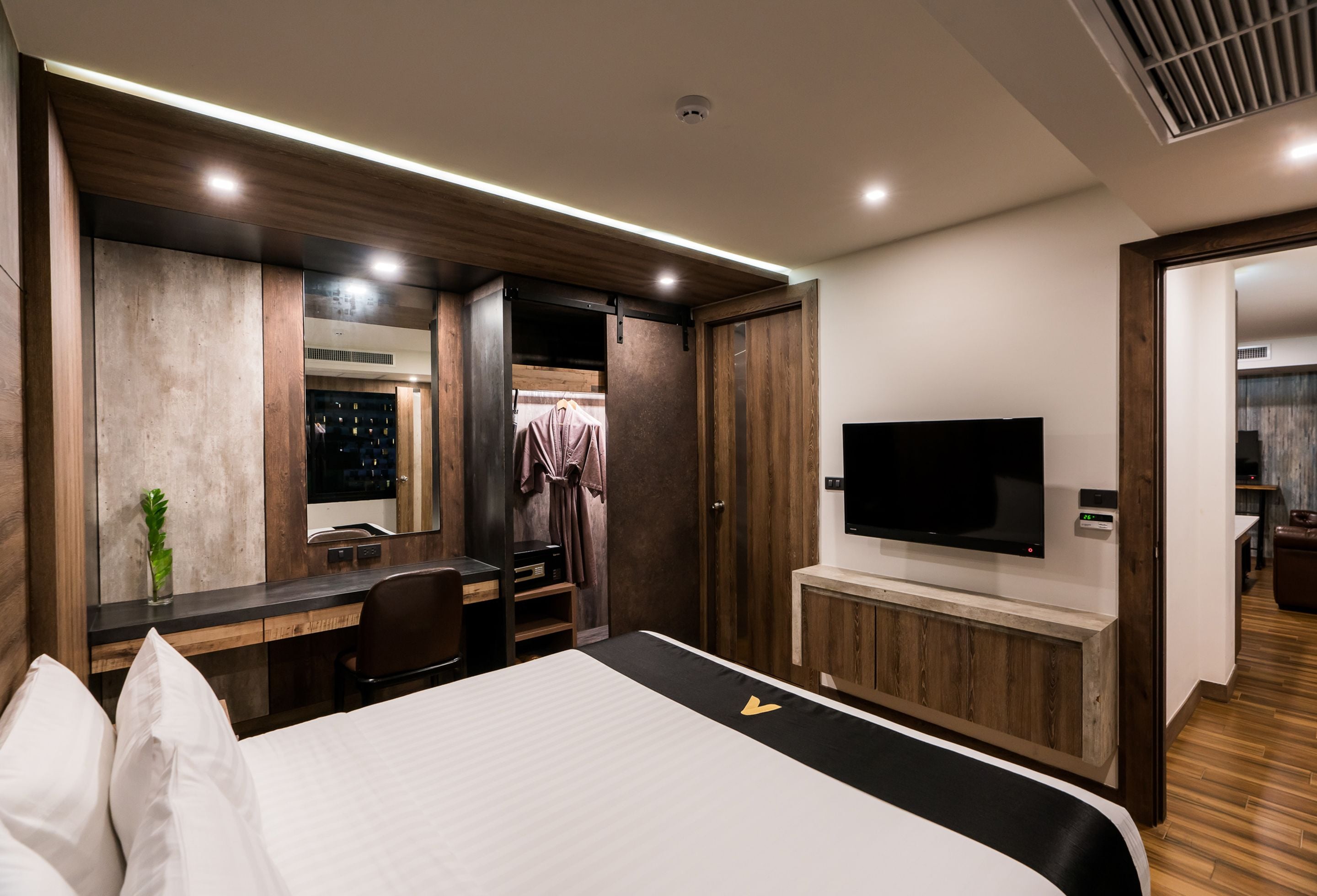 A modern hotel room with a large bed, a desk with a chair, a flat-screen TV, and a walk-in closet.