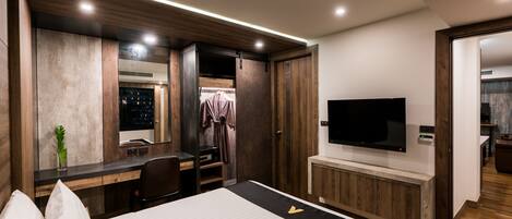 A modern hotel room with a large bed, a desk with a chair, a flat-screen TV, and a walk-in closet.