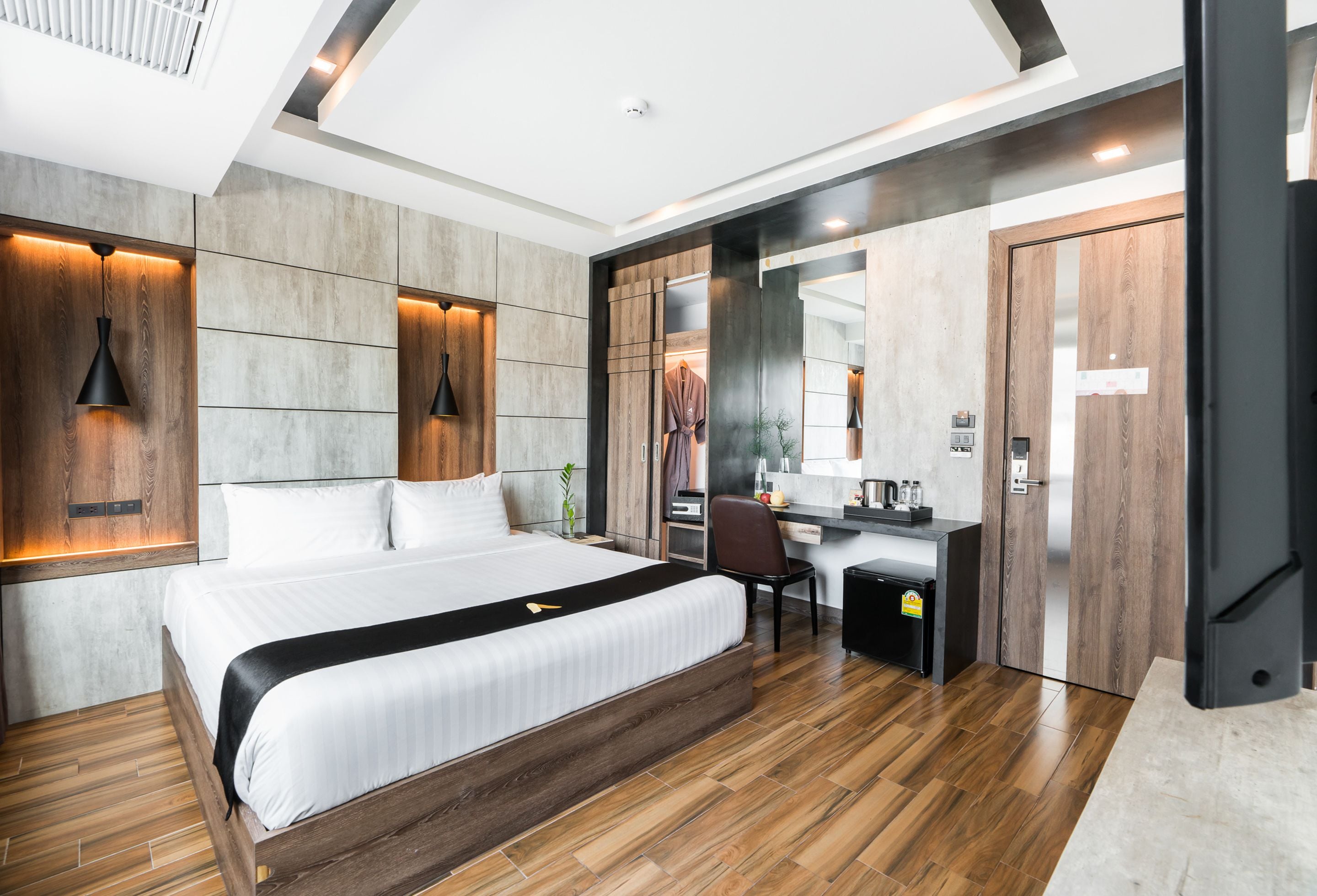 A modern hotel room with a large bed, a desk, and a wardrobe.