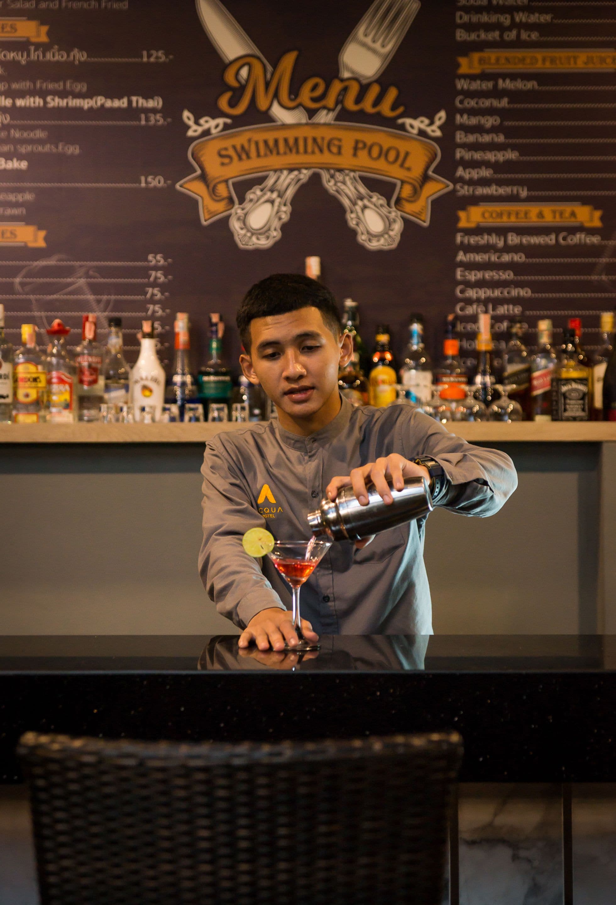 A bartender preparing a drink at a bar with a menu in the background.