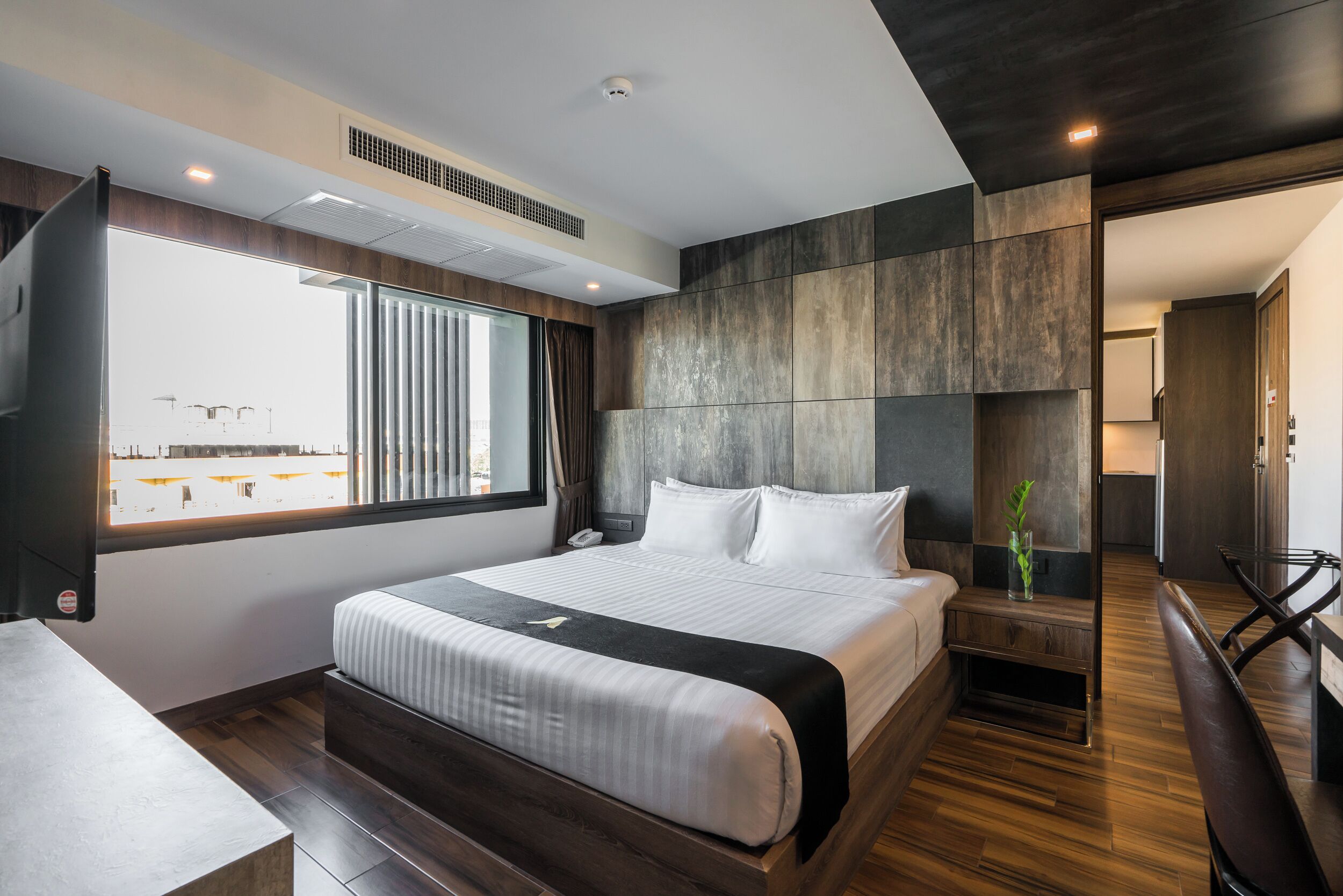 A modern hotel room with a large bed, a desk, and a view of the cityscape.