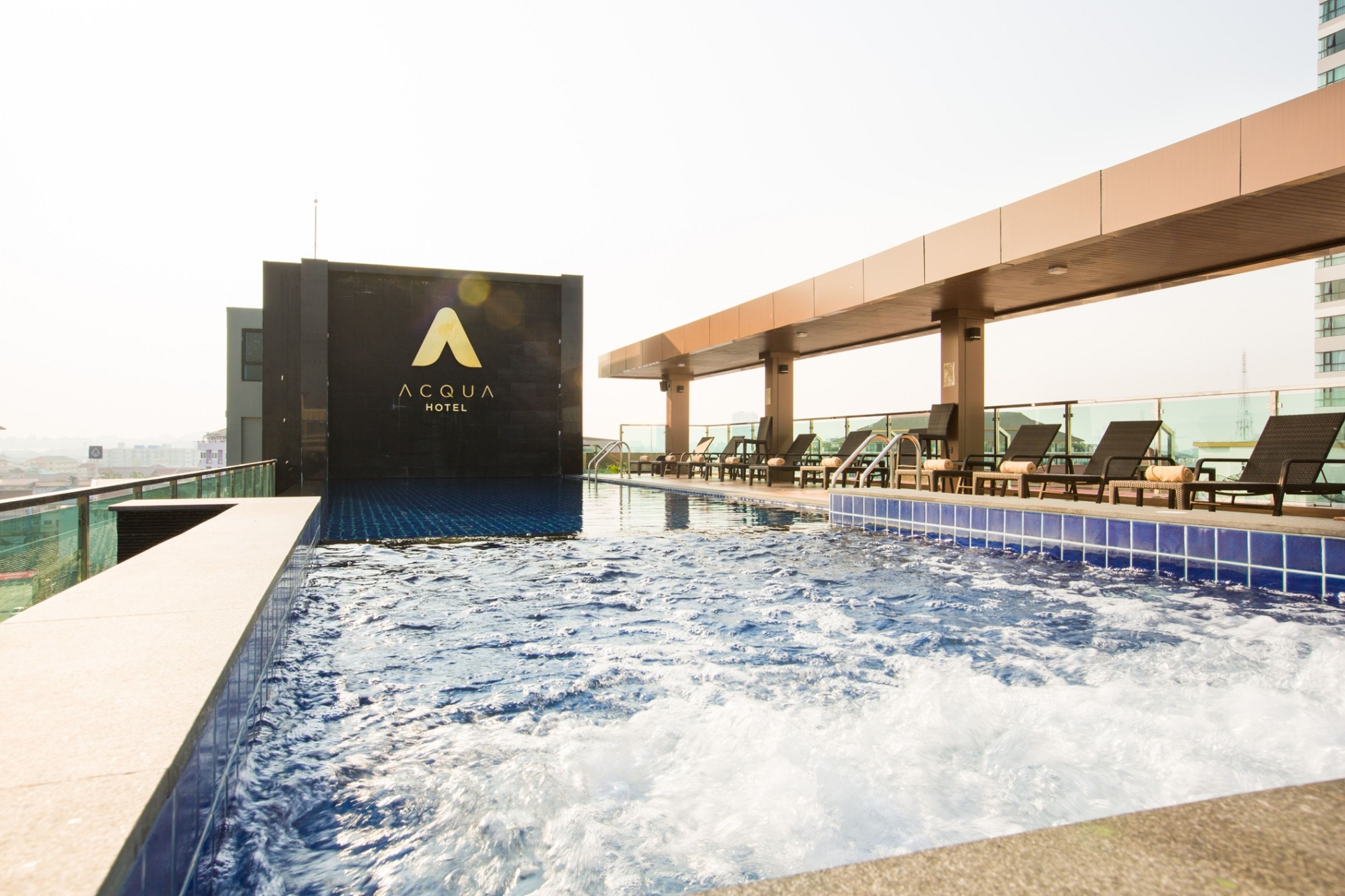 Une piscine sur le toit, agrémentée d’un panneau indiquant « Aqua Hotel », de chaises longues et offrant une vue sur la ville.