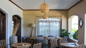 A dining area with wicker chairs, a round table, and a hanging light fixture. - Sunrise Hotel (Samos)