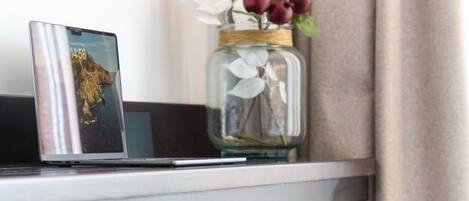 Una computadora portátil sobre un escritorio blanco, un florero con flores y una silla de madera.